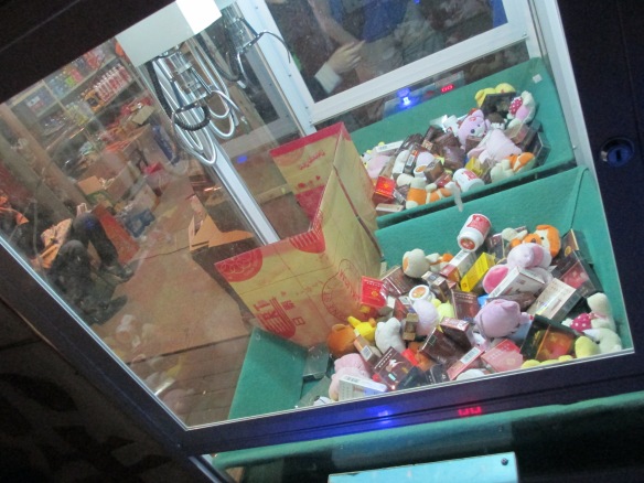 Claw machine containing an eclectic mix of teddy bears, chewing gum and cigarettes